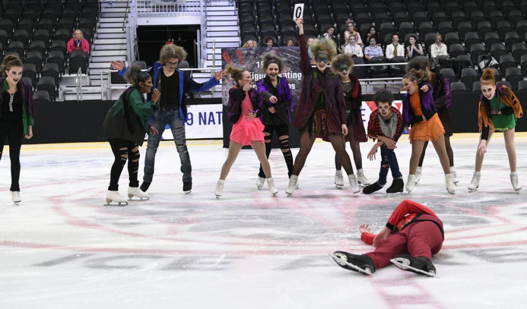 Intermediate Thriller skaters laughing at boy lying on ice.